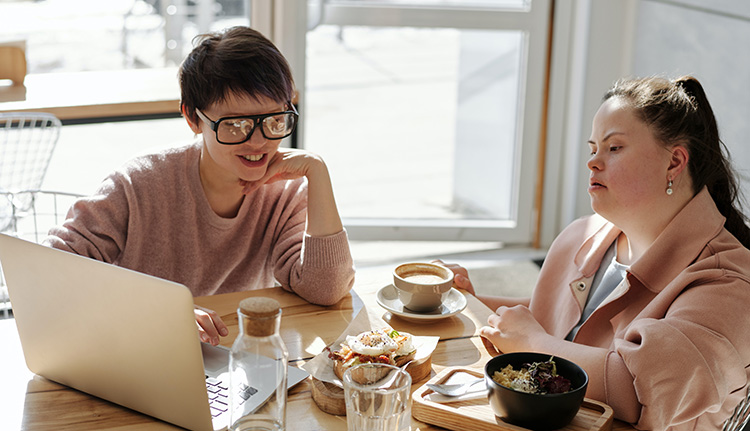 Two people with coffee cups look at a laptop computer.