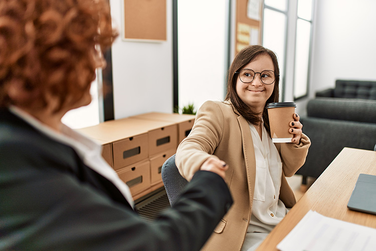Young woman drinks coffee and shakes hands with a colleague .
