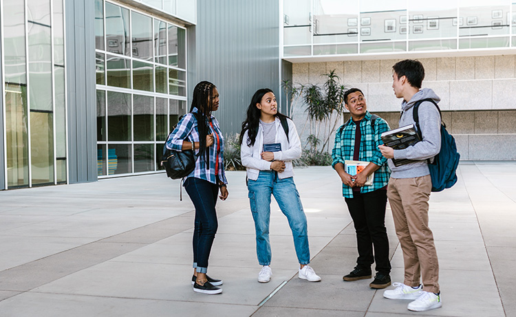 College students chat outside a large building.